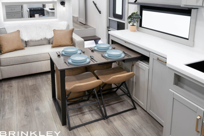 Brinkley Model Z Dinesk sliding desk-dining table shown in multiple configurations: extended as an L-shaped office desk, set as a dining table for four, and retracted for storage. Fits fifth wheel models 2670, 2680, & 2810. Features dark wood finish, sliding mechanism, and hidden storage drawers.