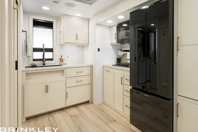| Model I 235 Travel Trailers 10 Kitchen interior of the Brinkley Model I 235 Travel Trailer showcasing high-quality construction details found in the best built travel trailers. Features include top-grade hardwood cabinetry with durable dovetail drawers, solid surface countertops, and an oversized stainless steel farmhouse sink. The space is illuminated by industry-exclusive square frameless Euro-styled windows with CraftSense™ hardwood trim, offering a residential look and superior ventilation.